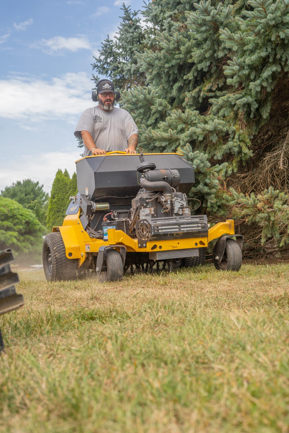 Operator running a stand-on aerator across a lawn