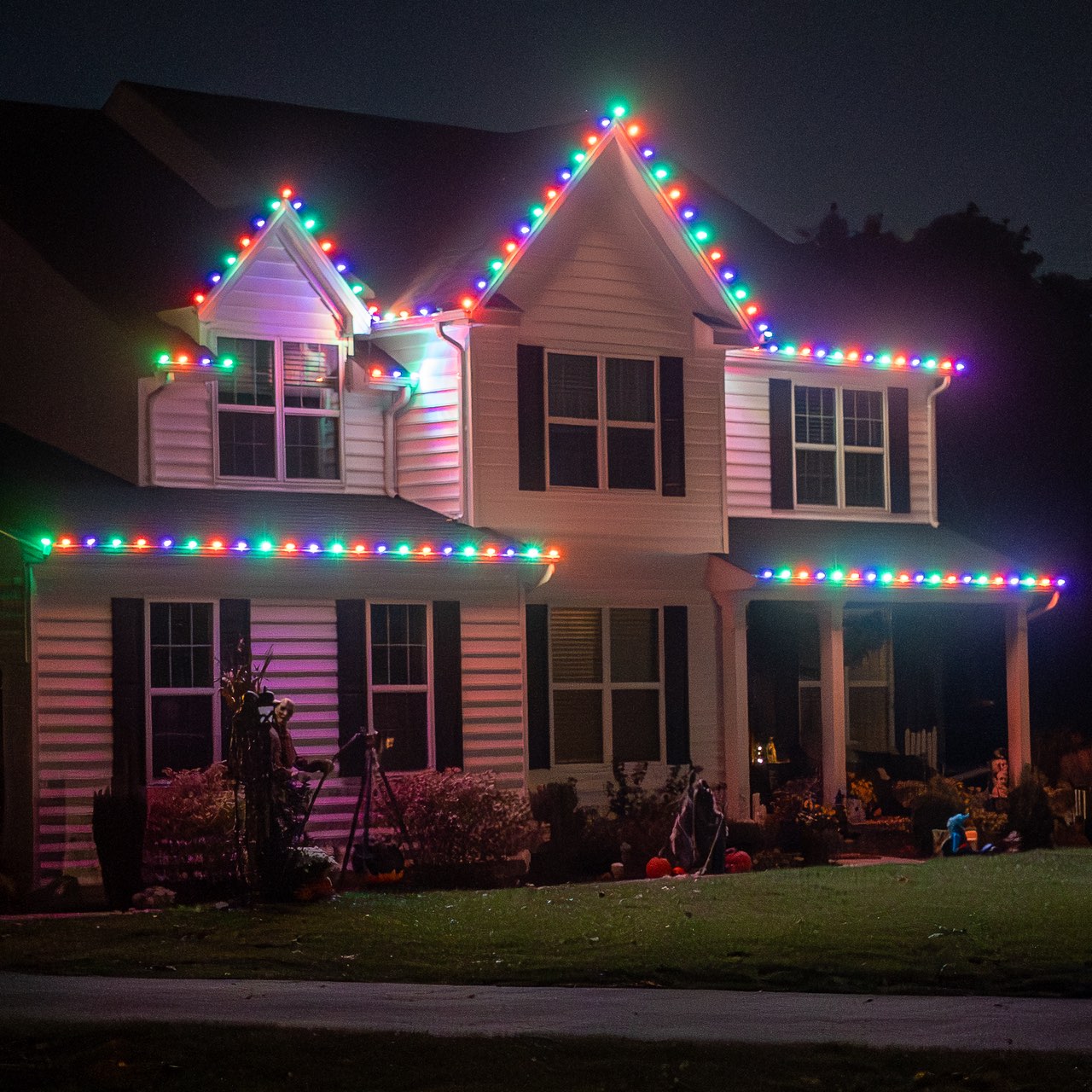 Two-story house at night with multicolor bulbs outlining both gables, the upper roofline and the porch, installed by Anderson Lawn Care