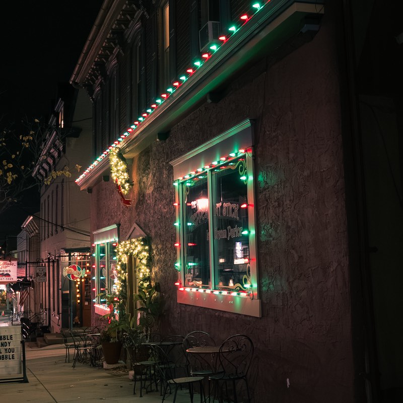 Main street storefront at night with red and green bulbs along the roofline and around the display windows